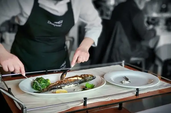 A chef cutting grilled fish on a table.